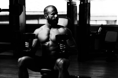 Sağlıklı bir adam karanlık bir spor salonunda omuzlarını çalıştırıyor.