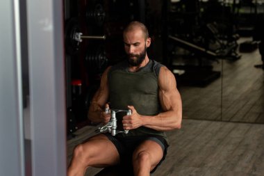 Kas geliştirme vücut geliştiricisi spor salonunda kablolu TV ile makineye dönmek için ağır ağırlık egzersizi yapıyor.