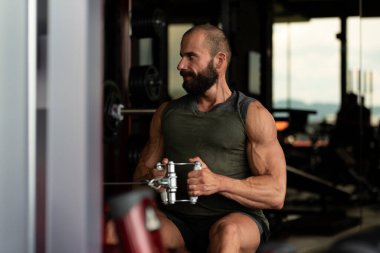 Kas geliştirme vücut geliştiricisi spor salonunda kablolu TV ile makineye dönmek için ağır ağırlık egzersizi yapıyor.
