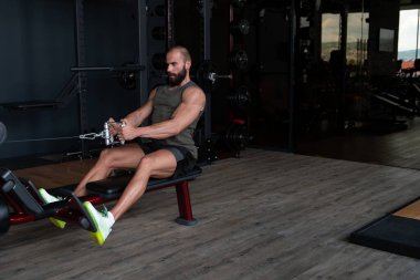 Kas geliştirme vücut geliştiricisi spor salonunda kablolu TV ile makineye dönmek için ağır ağırlık egzersizi yapıyor.