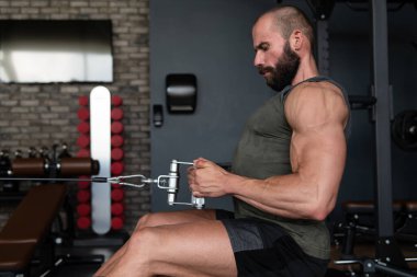 Kas geliştirme vücut geliştiricisi spor salonunda kablolu TV ile makineye dönmek için ağır ağırlık egzersizi yapıyor.