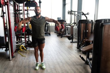 Kas Adam Spor Salonunda Dambıllı Omuzlar için Ağır Ağırlık Egzersizi Yapıyor