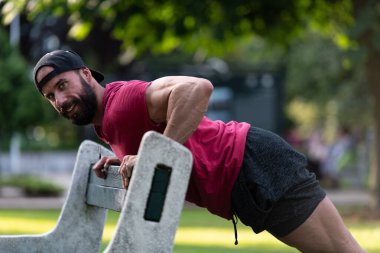 Kırmızı tişörtlü yakışıklı genç Park Bench 'te şınav çekiyor.