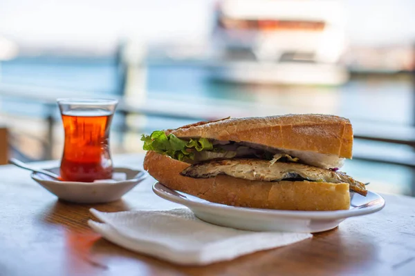 Sándwich de pescado de Estambul. Hamburguesa con pescado frito. Té turco con Balik Ekmek. Fondo borroso con vista al mar Imagen De Stock