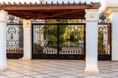 Güzel bir kapı ve arkadaki tropik yemyeşil alan. Sütunlar ve işlenmiş demir çitler. Lüks yerlere zengin dekoratif girişler zincir ile kilitlenir..