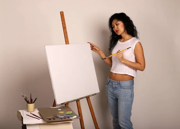 The artist at the easel paints a picture. Attractive girl with a brush paints. A blank canvas for a new painting and an artist with a brush and paints.