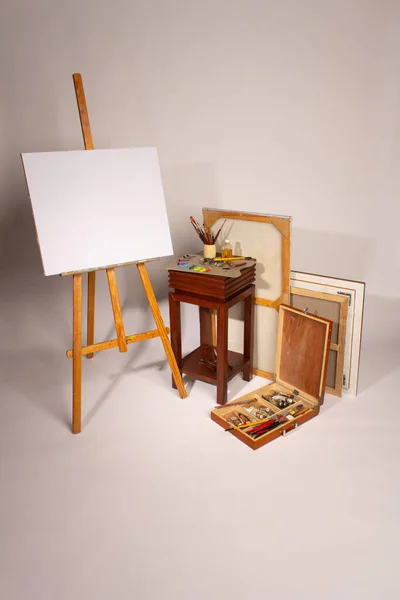 Oil painting. Blank canvas on Easel. Palette with paints and brushes. Squeeze out oil paints on a palette. Clean cloth with copy space. Set of brushes in a cup. Subframes and drawing tools