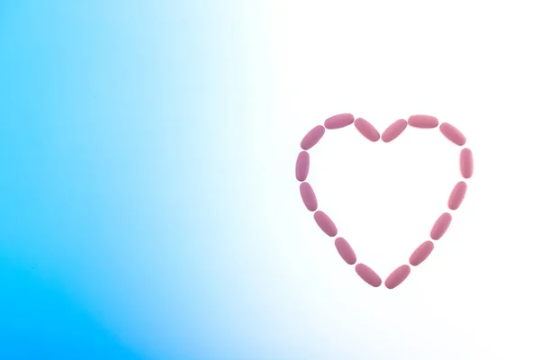 핑크 알약은 파란색 바탕에 심장 모양을 하고 있습니다. 치료를 위한 알약으로 만들어 진 심장 모양, 치료와 건강 관리에 대한 개념. 오른쪽 심장, 왼쪽에 복사 공간. — 스톡 사진