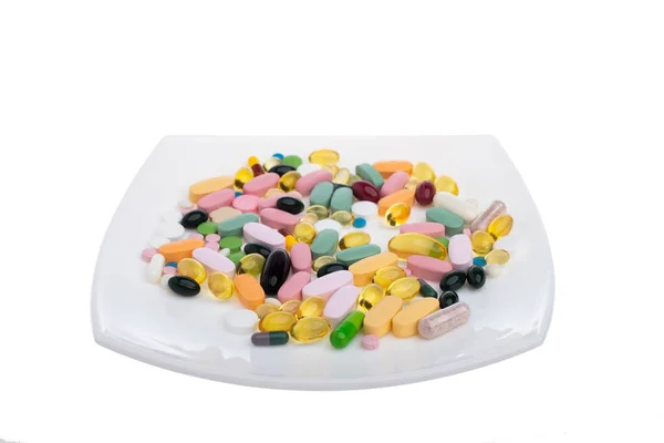 Una pila de píldoras multicolores en un plato blanco que simboliza la comida. Vitaminas sobre un fondo blanco aislado. Diferentes medicamentos. Tabletas y pastillas de diferentes formas y colores . — Foto de Stock