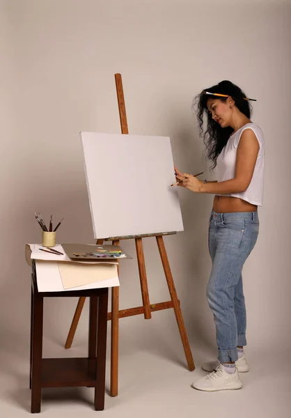 The artist at the easel paints a picture. Attractive girl with a brush paints. A blank canvas for a new painting and an artist with a brush and paints.