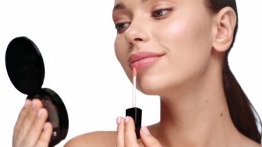 Gülümseyen kadın beyaza izole edilmiş dudak kremi sürüyor.