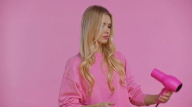 Kadın saçlarını kurutuyor ve pembe üzerinde gülümsüyor.