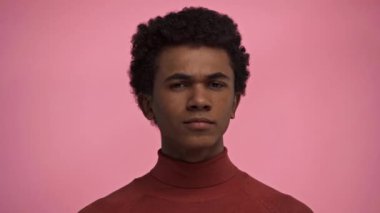 Afro-Amerikalı genç pembe kameraya bakıyor.