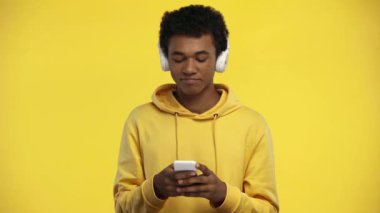 Afro-Amerikan ergen, sarıda izole edilmiş akıllı telefon kullanıyor.