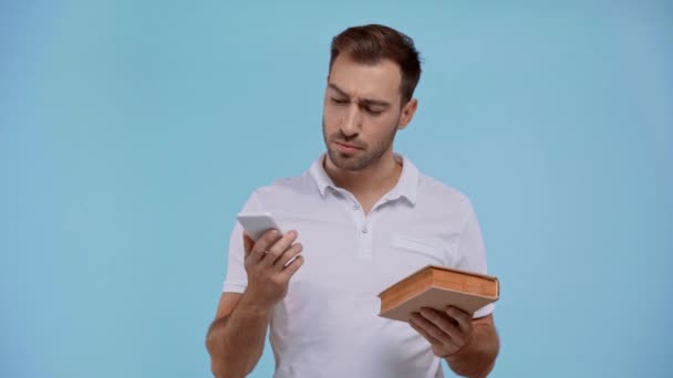 Hombre Pensativo Sosteniendo Libro Teléfono Inteligente Aislado Azul — Vídeo de stock