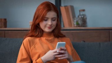 Düşünceli kızıl saçlı genç kız akıllı telefondan konuşuyor.