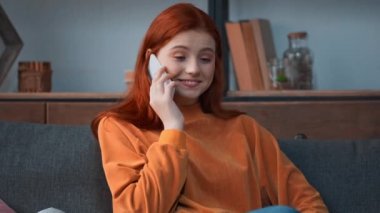 Gülümseyen kızıl saçlı genç kız akıllı telefondan konuşuyor.
