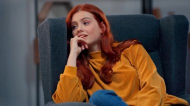 Pozitif kızıl saçlı genç kadın koltukta oturuyor.