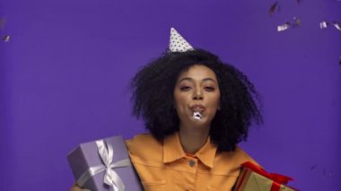 Afro-Amerikalı kadın parti kornasını çalıyor. Mor renkte izole edilmiş. 