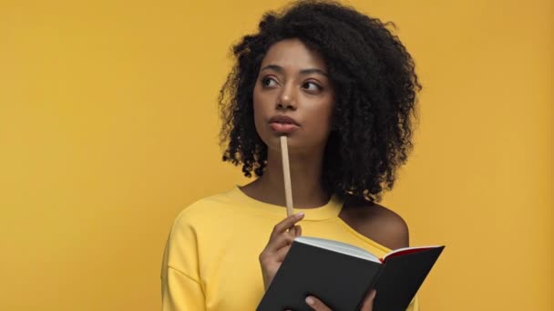 Nachdenkliche Afroamerikanerin Schreibt Notizbuch Isoliert Auf Gelb — Stockvideo