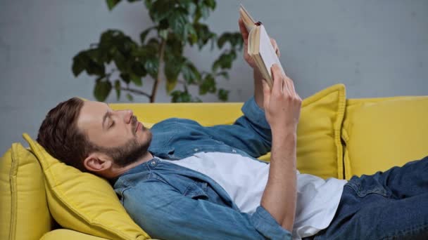 Concentrated Man Reading Book While Lying Sofa — Stock Video