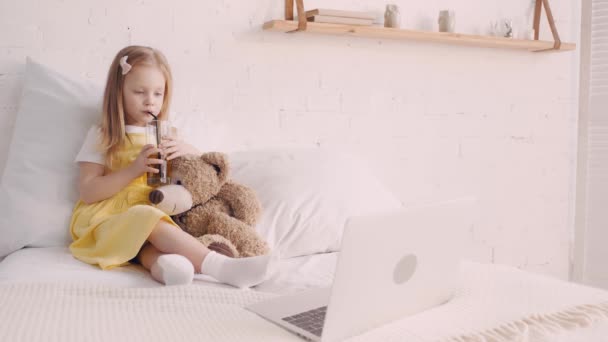 Kind Trinkt Saft Von Teddybär Während Laptop Bett Film Schaut — Stockvideo