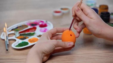 cropped view of woman painting orange easter egg 