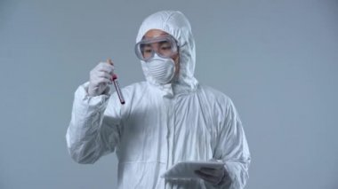 Asyalı bilim adamı dijital tablet ve koronavirüs virüsü örneği tutuyor. Gri harflerle izole edilmiş. 