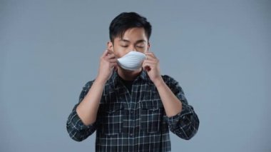 Mutlu Asyalı adam gri üzerine izole edilmiş koruyucu maskeyi çıkarıyor. 