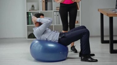 Fitness topunda karın kası yapan iş adamının yakınındaki spor eğitmeninin kırpılmış görüntüsü