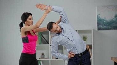 Çekici fitness eğitmeni, iş adamına ofiste egzersiz yaptırıyor. 