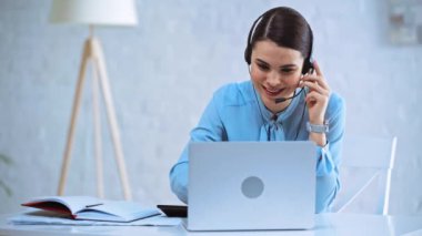 Kulaklıklı mutlu operatör konuşuyor ve dizüstü bilgisayar kullanıyor 