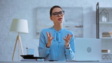 çekici iş kadını konuşuyor ve dizüstü bilgisayarın yanında el kol hareketi yapıyor.