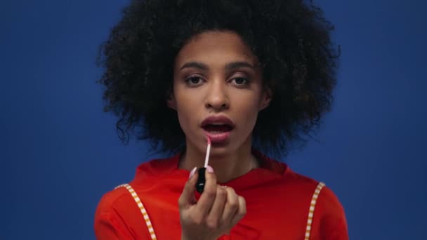 Krullend Afrikaans Amerikaans Meisje Toepassen Lip Gloss Geïsoleerd Blauw — Stockvideo