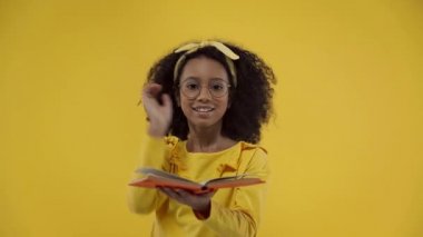 african american kid gesturing and holding book isolated on yellow 