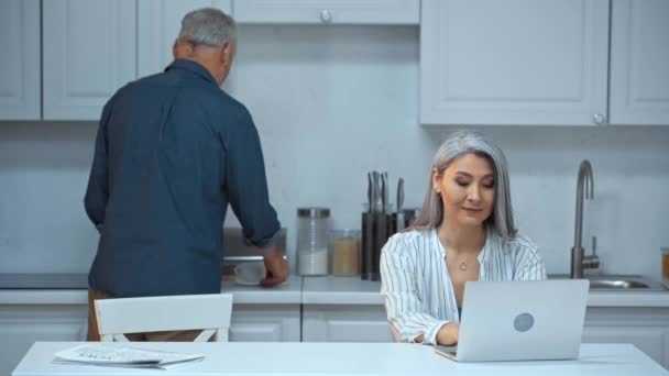 Sénior Hombre Con Tazas Café Cerca Asiático Esposa Con Laptop — Vídeo de stock