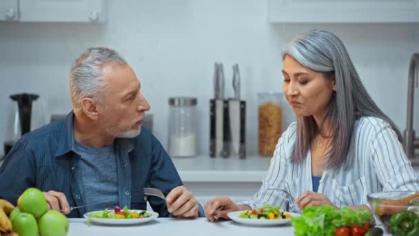 上級異人種間のカップルはキッチンでサラダを食べる — ストック動画