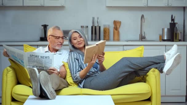 Feliz Asiático Mujer Leyendo Libro Cerca Senior Marido Con Periódico — Vídeo de stock