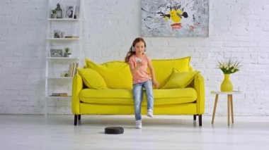 Kulaklıklı çocuk robot elektrik süpürgesinin yanında müzik dinliyor.