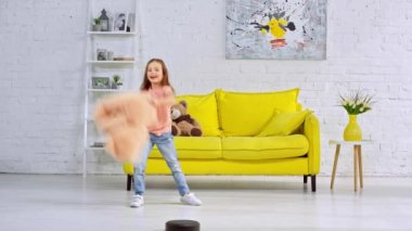 Robotik elektrik süpürgesinin yanında yumuşak oyuncaklarla oynayan mutlu çocuk.