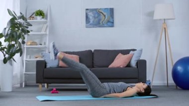 Spor kadını oturma odasındaki spor paspası üzerinde çalışırken yan görünüm