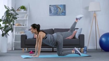 Gülümseyen sporcu kadının evde spor paspası üzerinde egzersiz yaparken yan görünümü