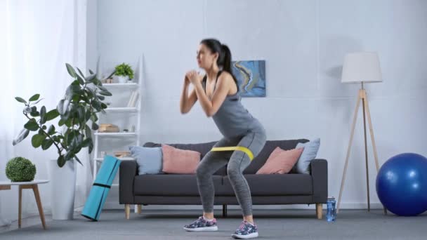 Deportiva Haciendo Sentadillas Con Banda Resistencia Mientras Entrena Casa — Vídeos de Stock