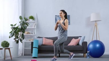 Spor kadını evdeki spor malzemelerinin yanında hamleler yapıyor.