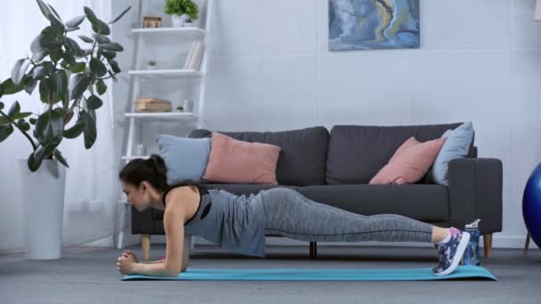 客厅里女运动员在健身垫上做跳板的侧视图 — 图库视频影像