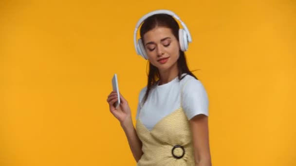 戴耳机的女孩跳舞 手里拿着用黄色隔开的智能手机 — 图库视频影像