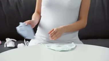 Hamile bir kadının yeni doğan kıyafetlerini masaya dizdiği görüntüler.