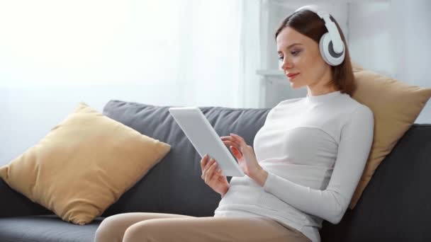 Έγκυος Γυναίκα Ακουστικά Που Χρησιμοποιεί Ψηφιακό Δισκίο Στον Καναπέ — Αρχείο Βίντεο