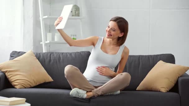 Glückliche Schwangere Mit Videoanruf Auf Digitalem Tablet Auf Der Couch — Stockvideo