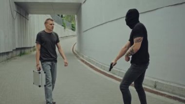 Dövmeli bir gangster, maskeli, silahlı ve bir adamla kavga ediyor.